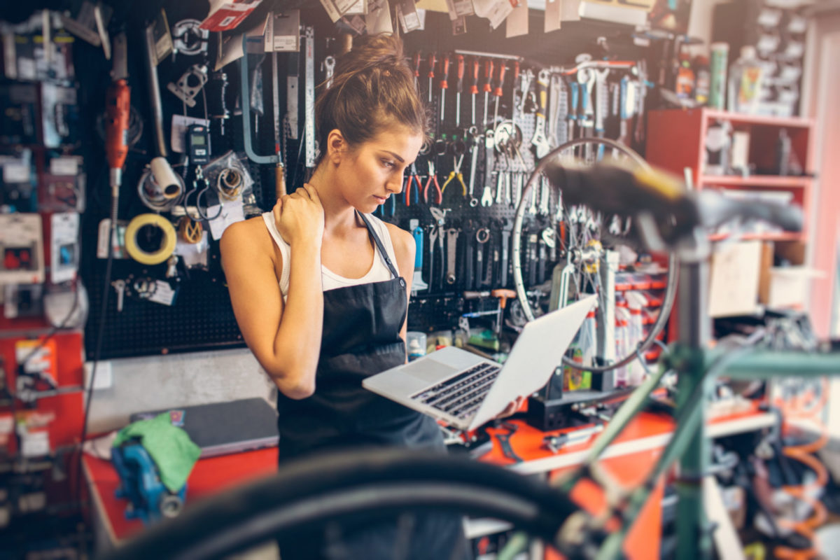 Portrait of a young female bicycle mechanic using a laptop.